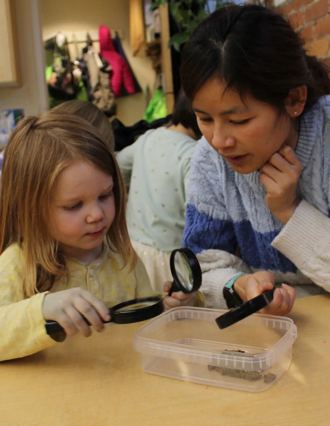 A child and teacher looking at a specimen through magnifying glasses at Cambridge-Ellis School