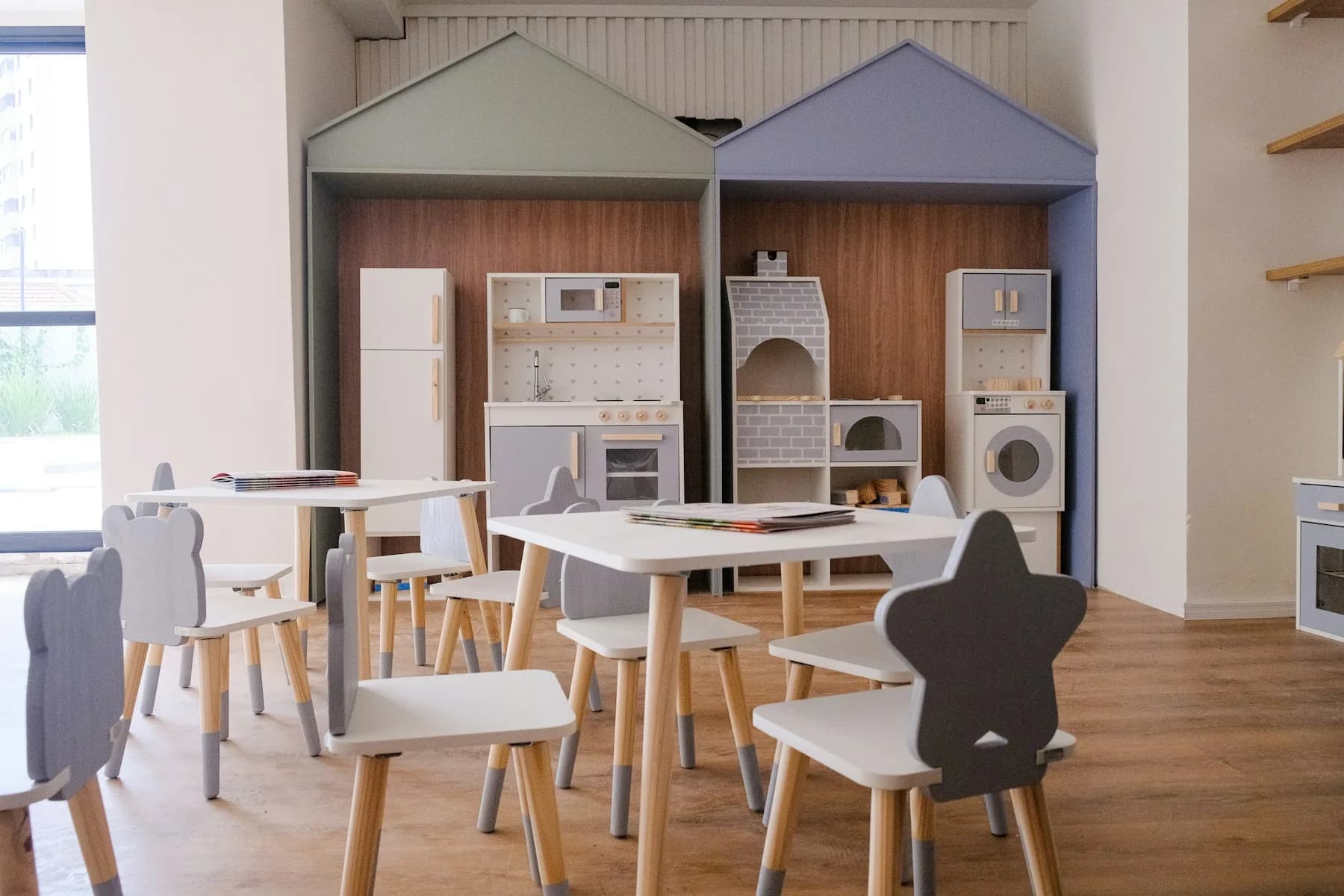A bright children's play area with small tables, star-shaped chairs and toy kitchens.