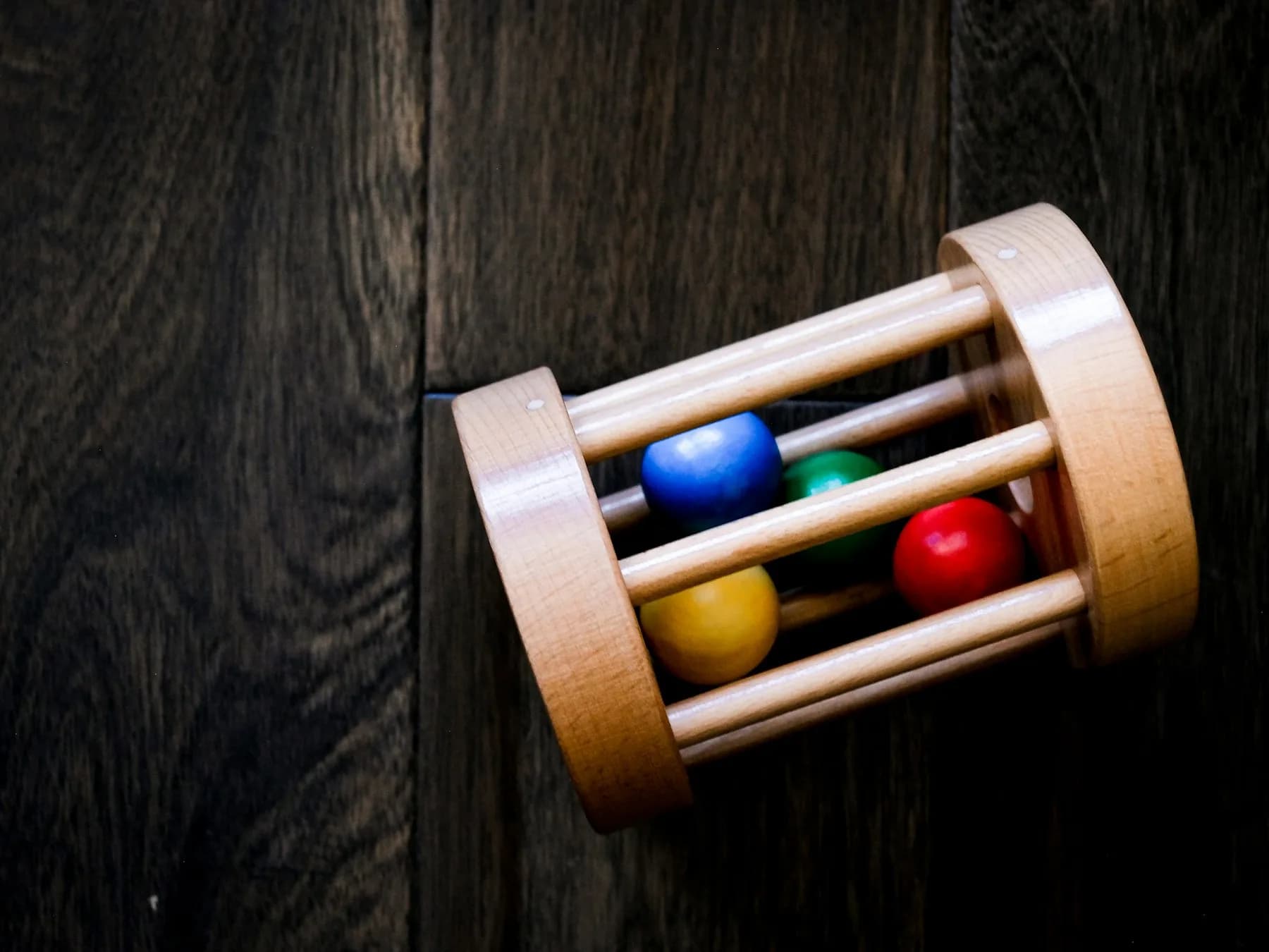 A wooden rolling toy with coloured balls on a dark wooden floor.