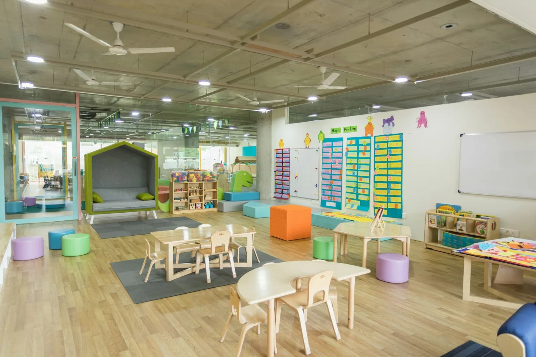 A bright early-years classroom with small tables, reading shelves and wooden floors.