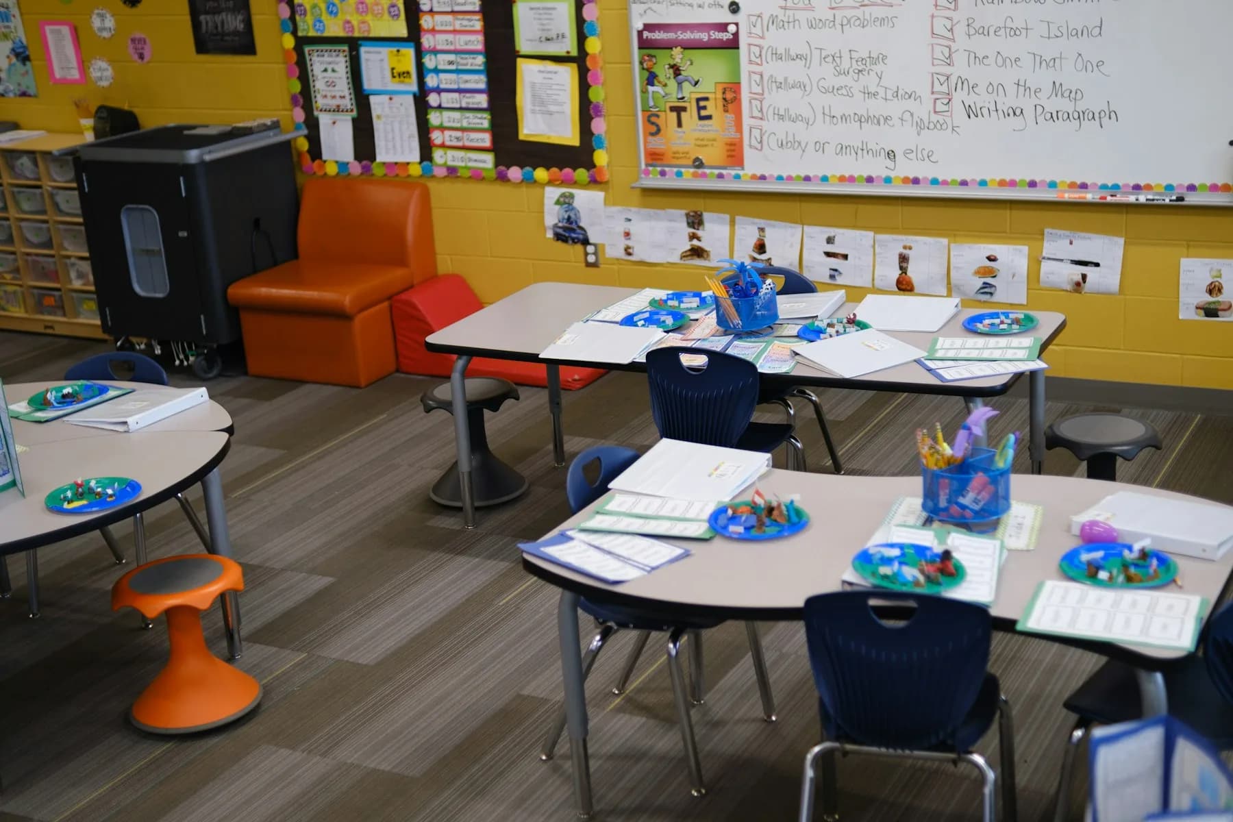 Tables with blue chairs and student materials in a colourful elementary classroom.
