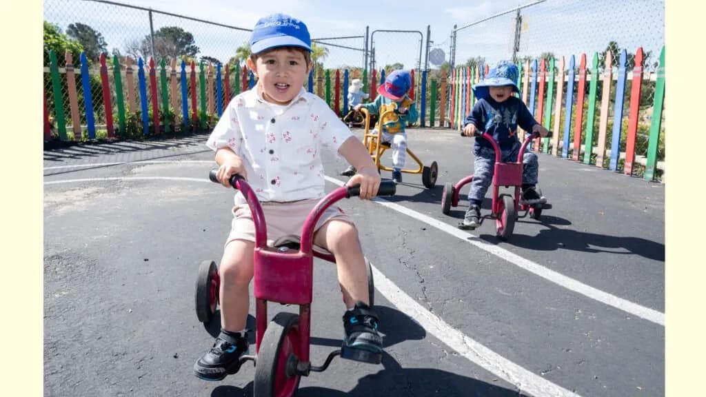 Two children riding tricycles on the play yard at Tsumiki Preschool