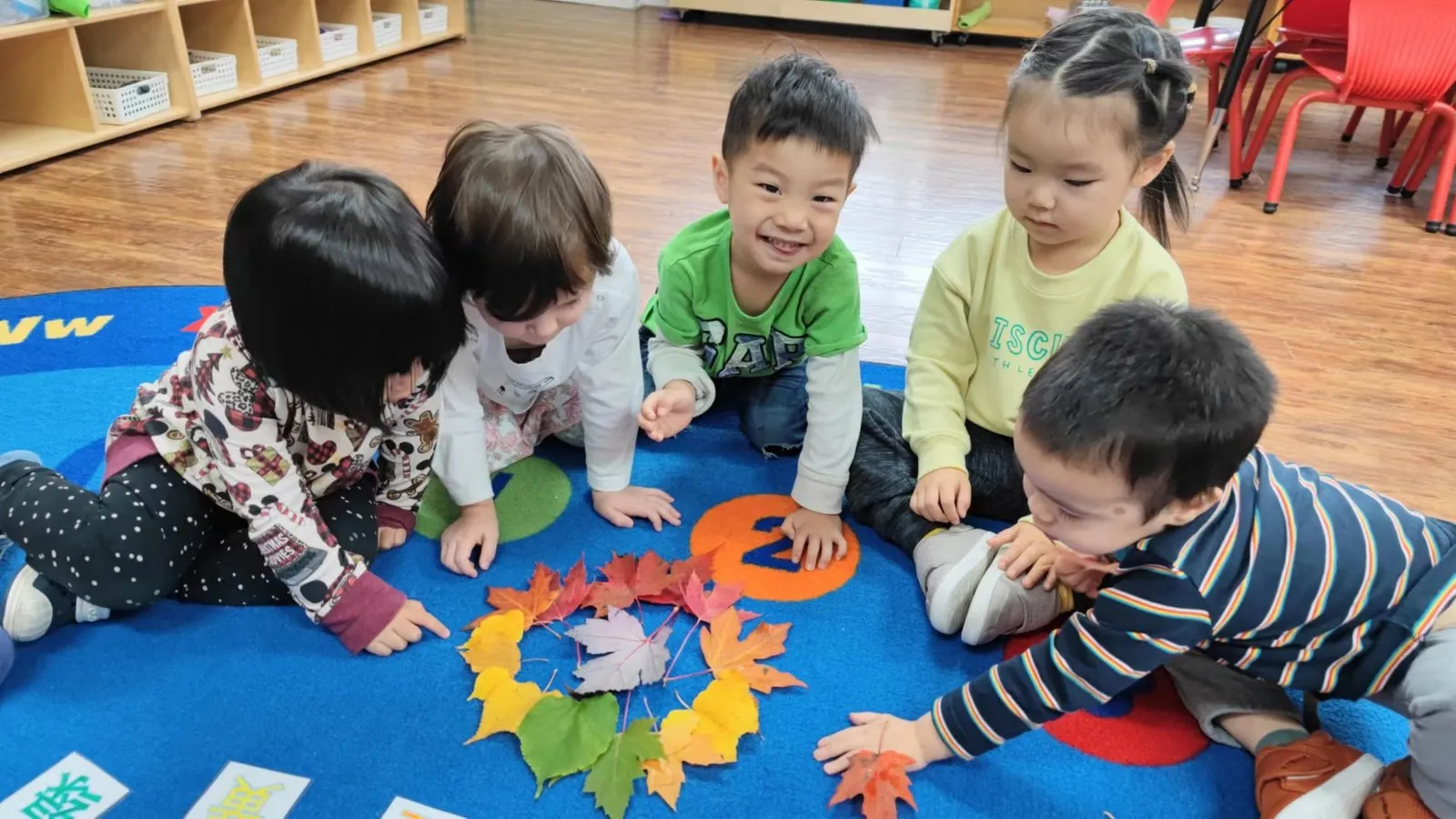 Children arranging autumn leaves on a classroom rug at Jingbao Bilingual