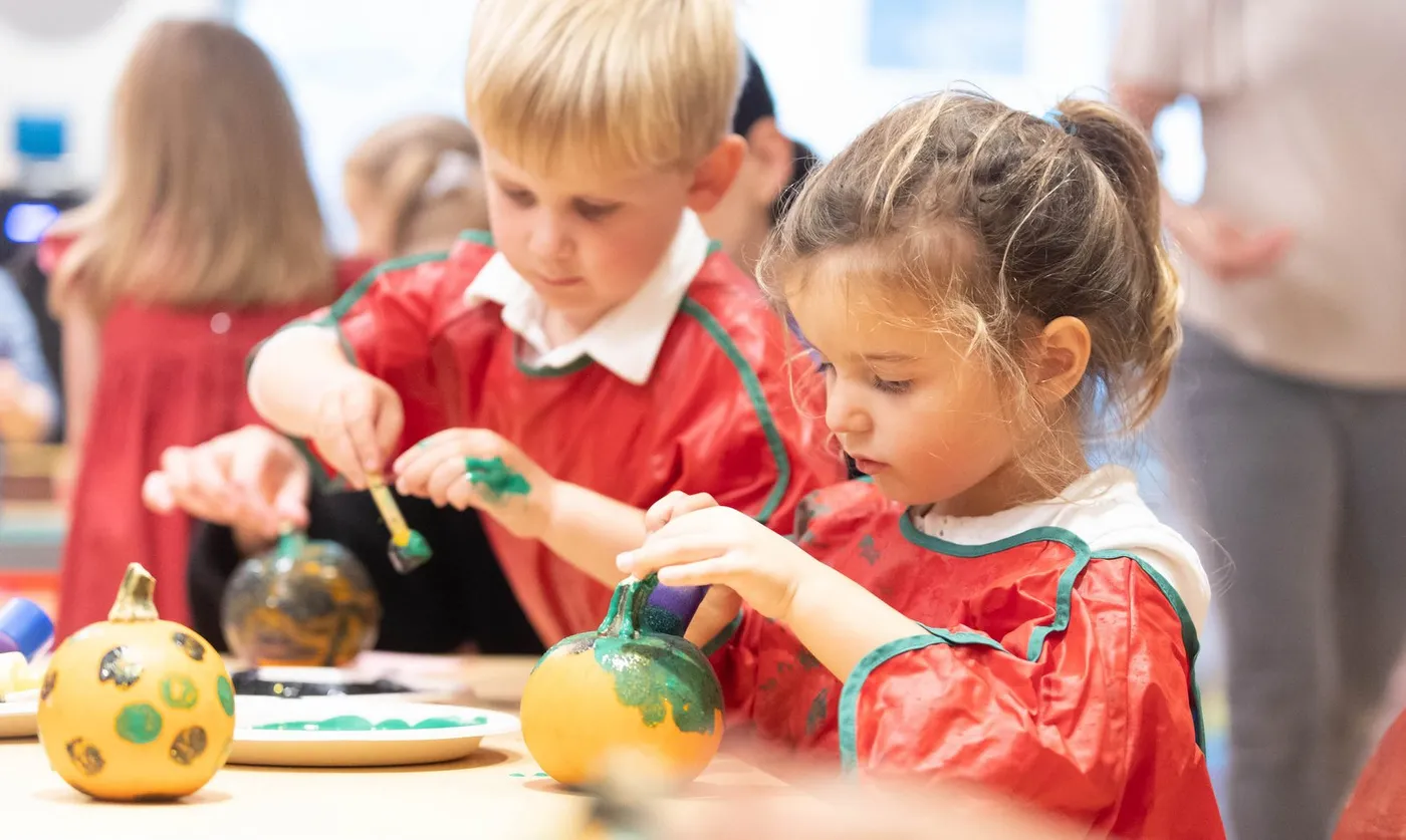 Two children painting objects in red aprons at Spruce Street Nursery School