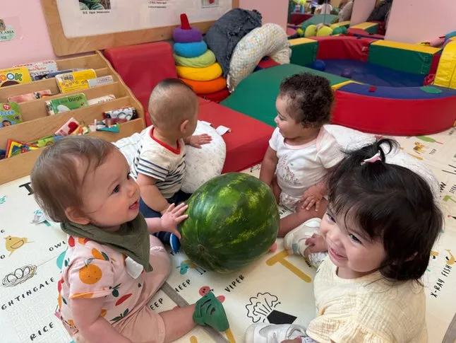 Infants playing on a floor mat with a toy watermelon at Buds & Blossoms