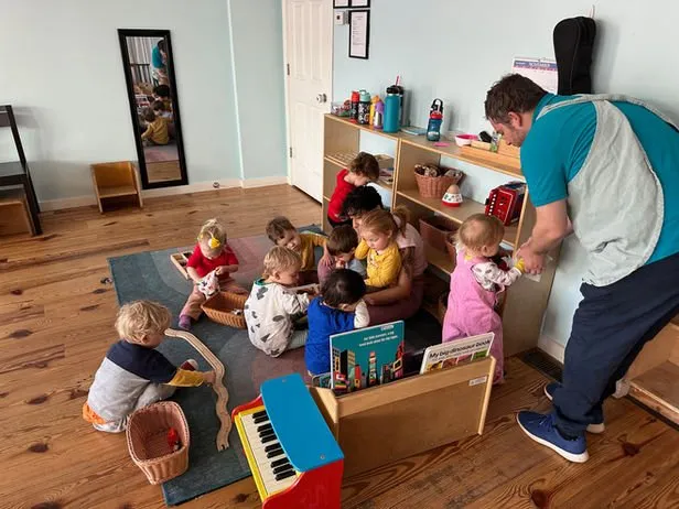 Toddlers gathered with a teacher near a piano in a Montessori classroom at Snapdragon Montessori School