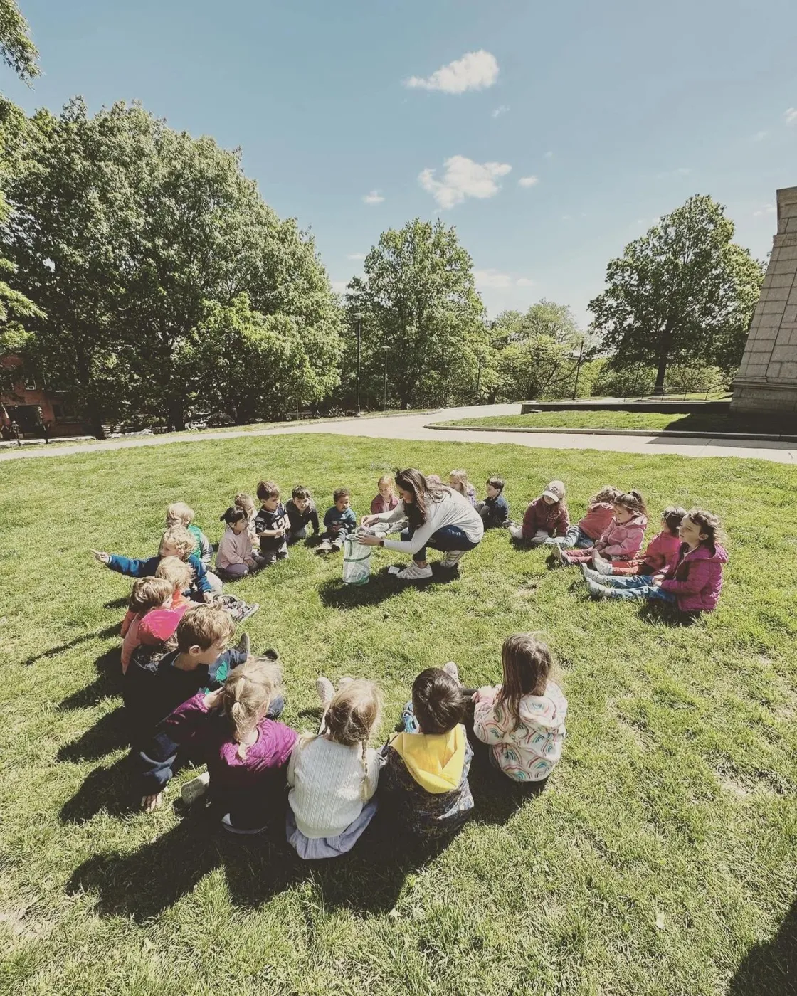 Children and a teacher sitting in a circle on the grass at The Treehouse School in Charlestown