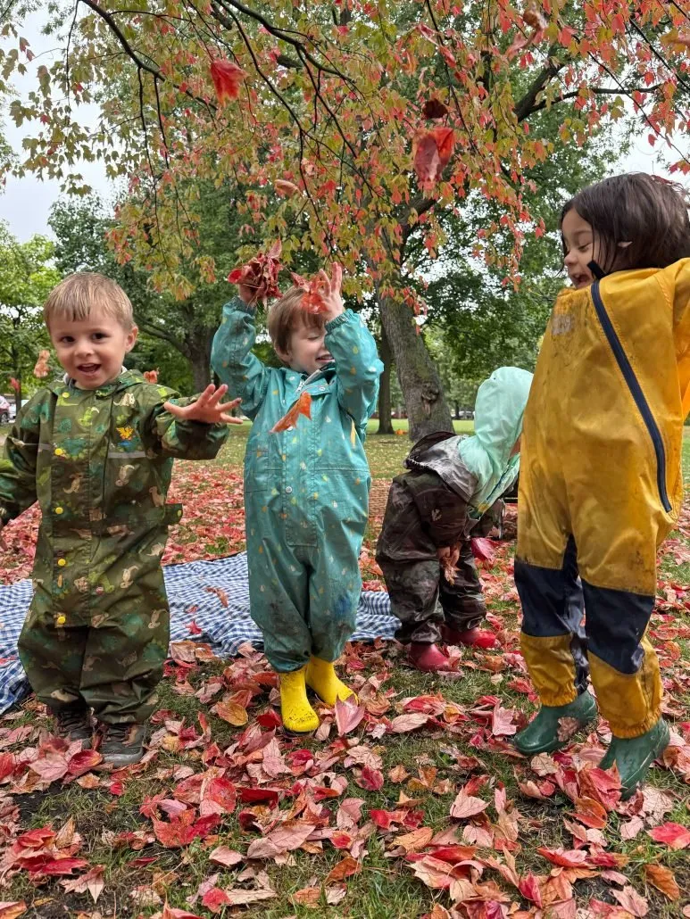 Toddlers in rain gear playing in fallen leaves near Stepping Stones Nursery School