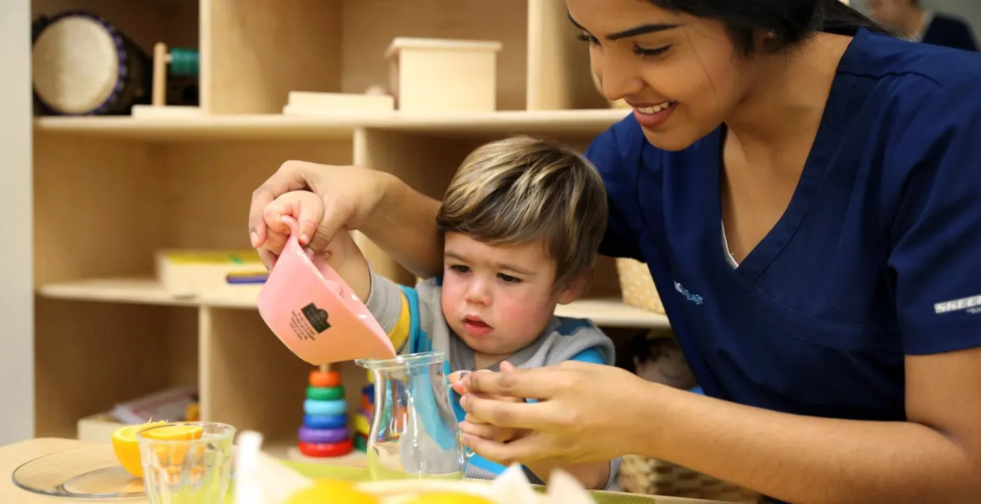Teacher helping a toddler pour water in a Living the Language classroom