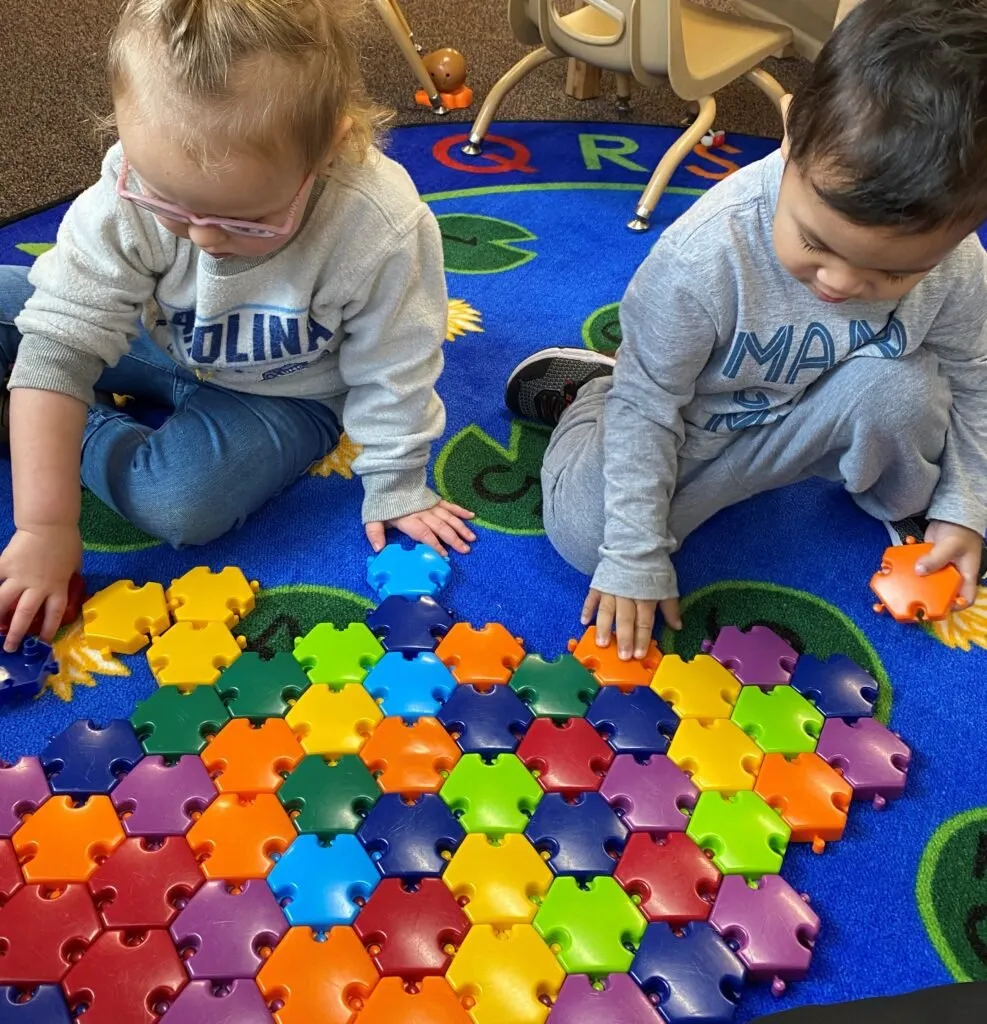 Two children building with colourful connecting tiles on a classroom rug at Como Early Learning Center