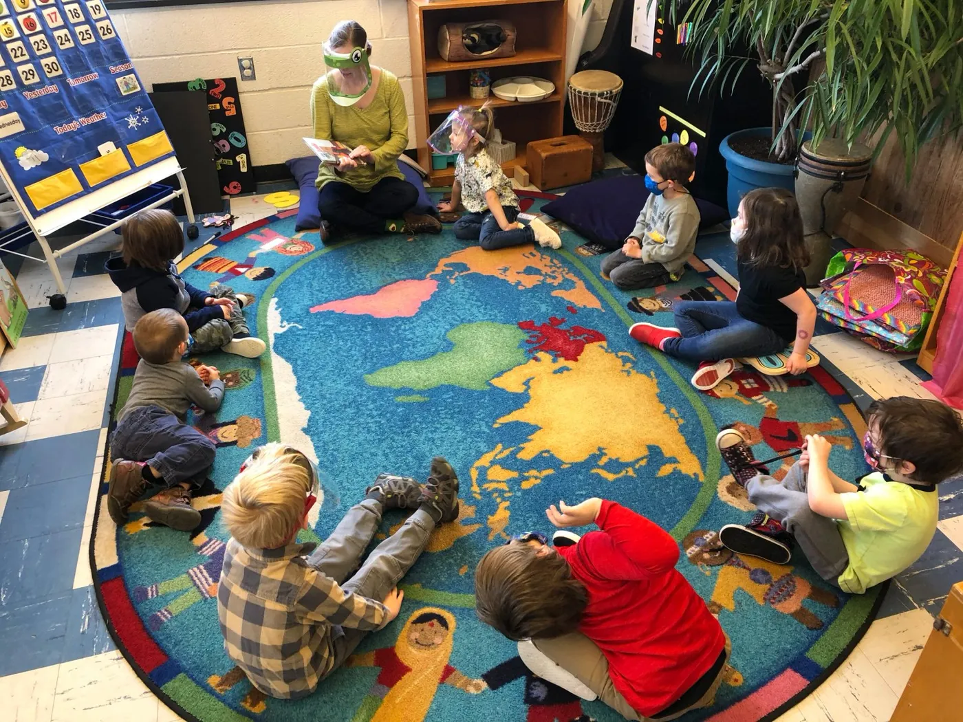 Children sitting in a circle on a world map rug with a teacher at Bright Prospects Cooperative Preschool