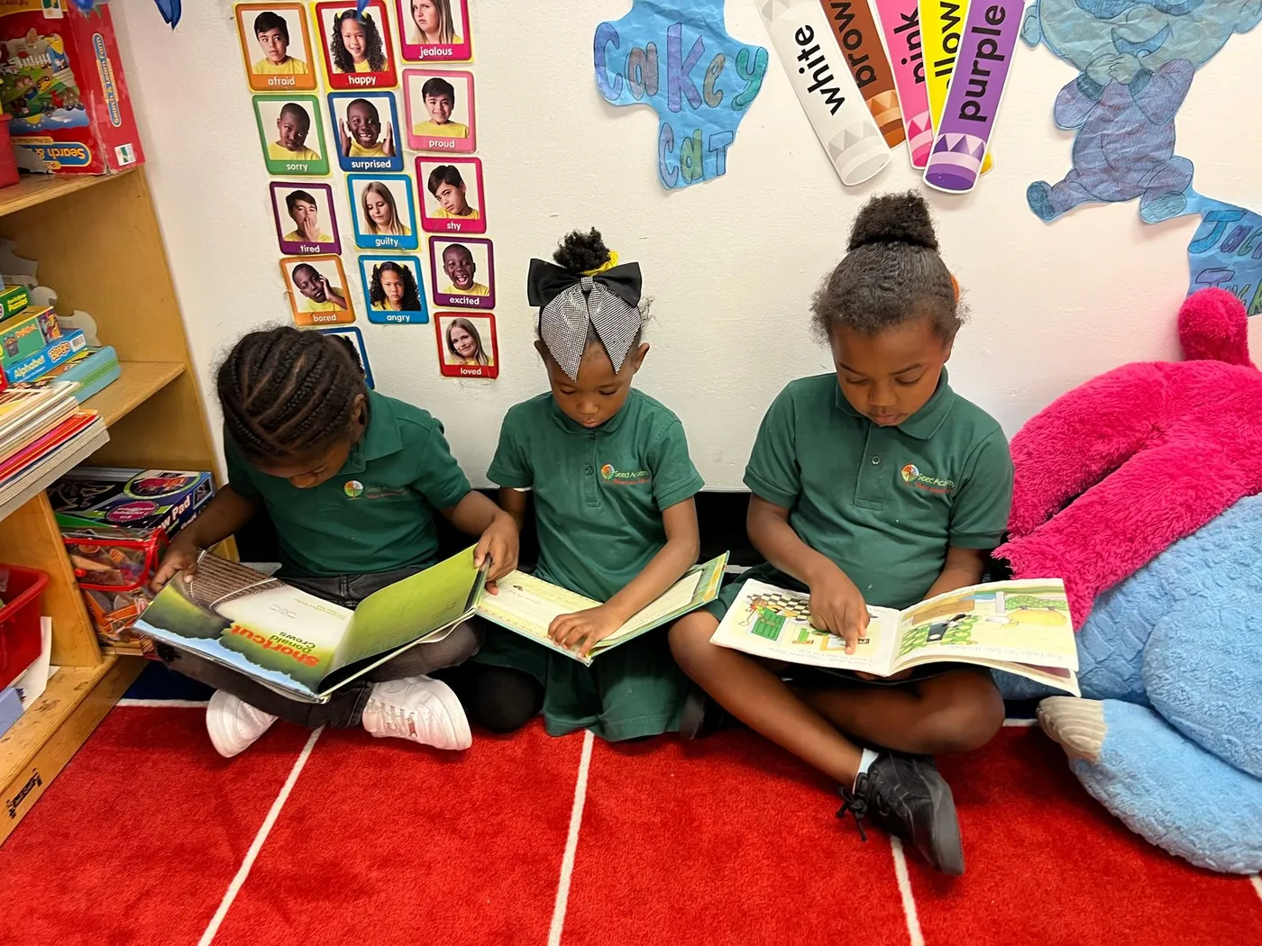 Three children in school uniforms reading picture books on a red rug at Seed Early Learning Academy