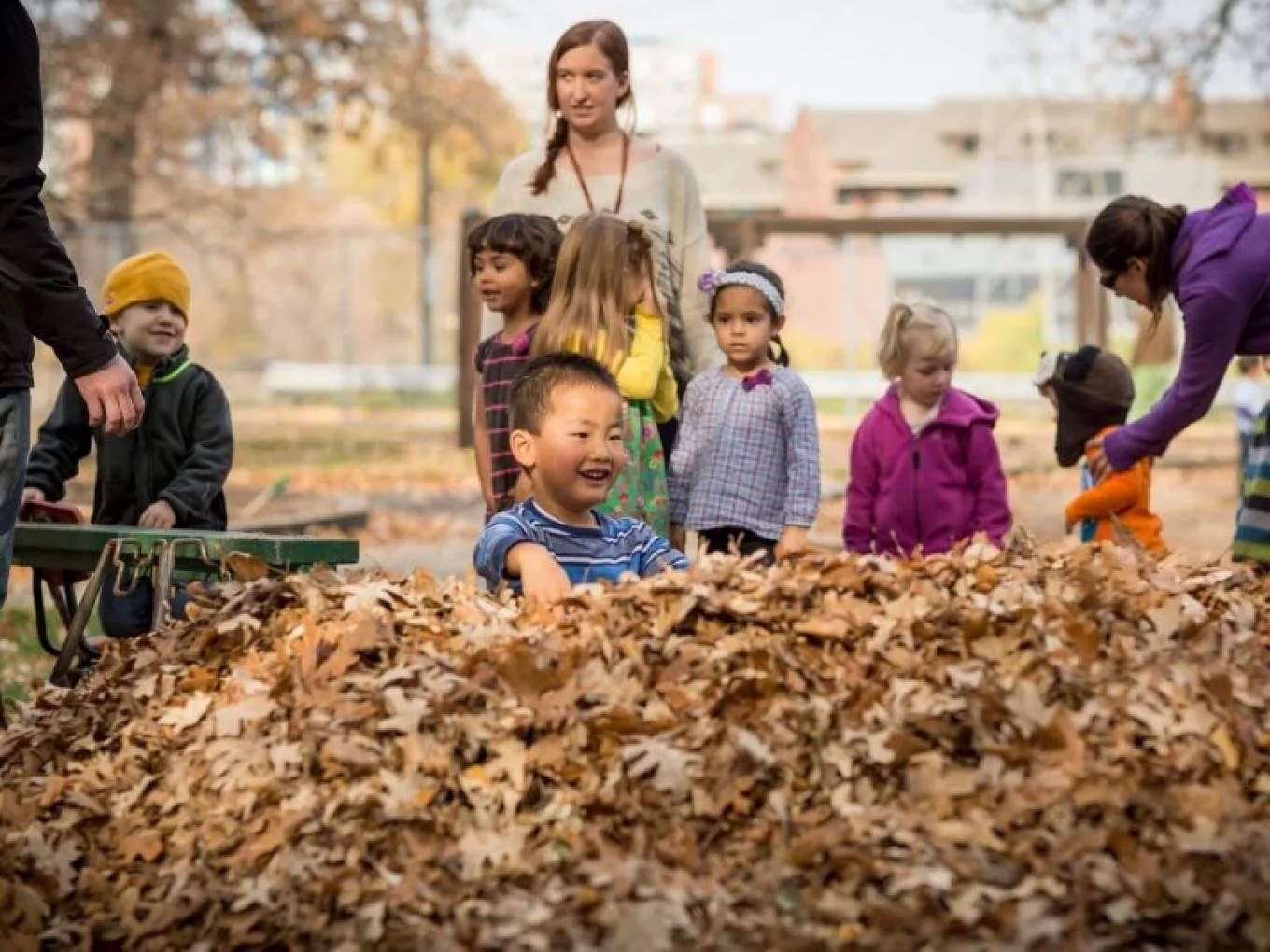 Children and teachers gathered around a pile of autumn leaves at the Child Development Laboratory School