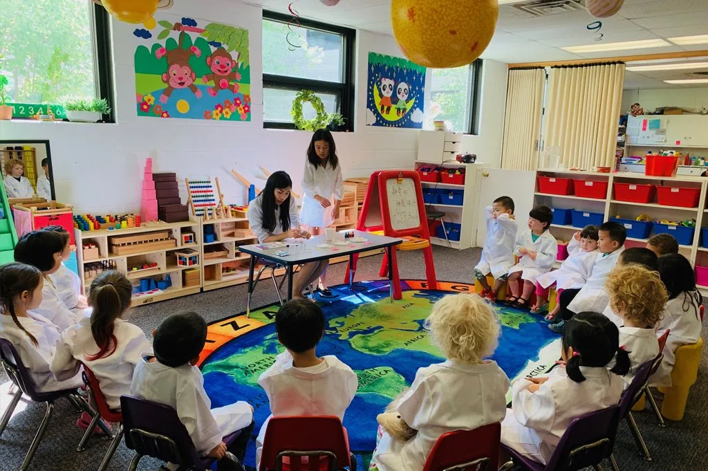 Children in white coats sitting in a circle on a world map rug with a teacher at Minnesota Chinese Daycare