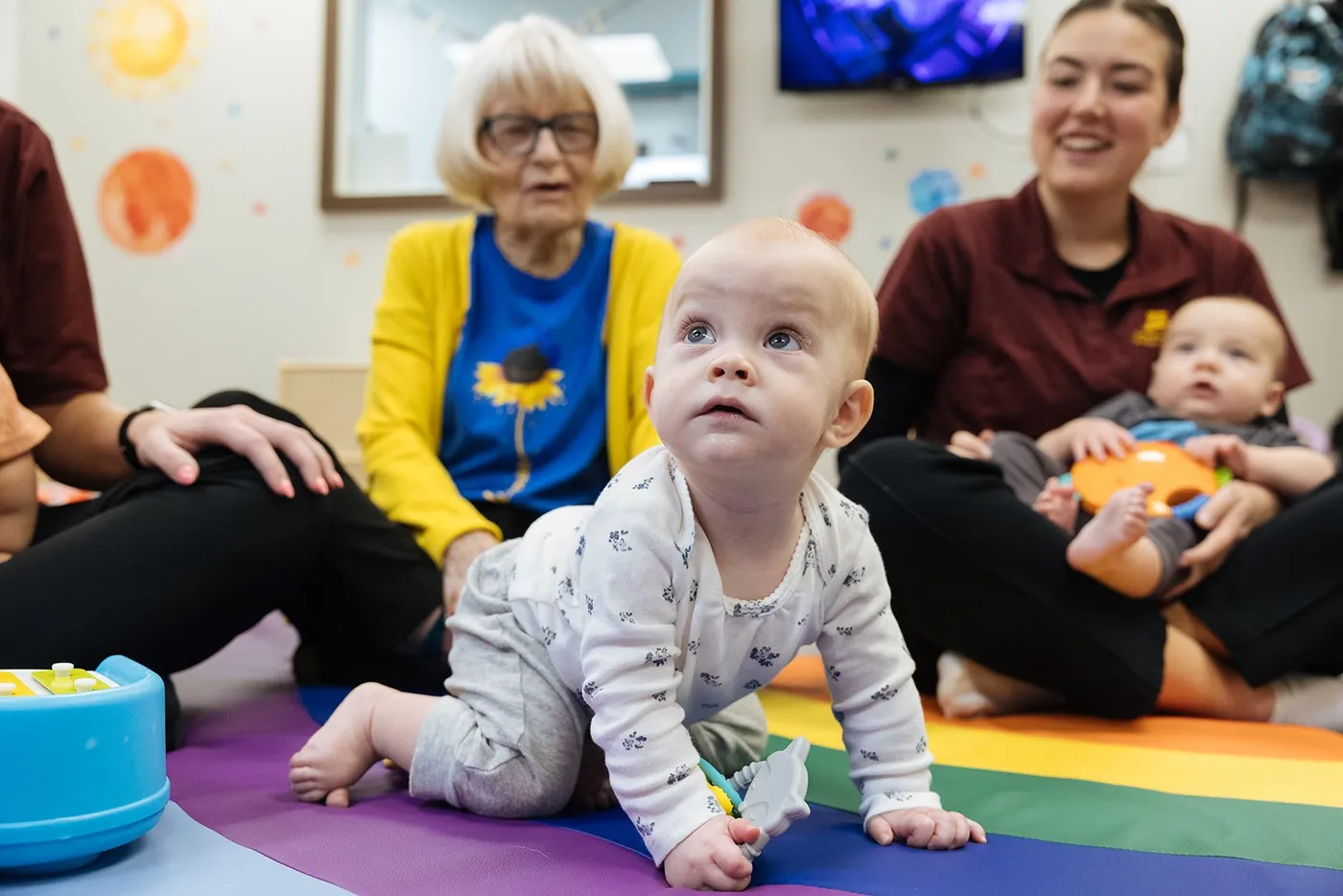 A baby on a play mat with an older resident and a teacher at The Pillars Child Care