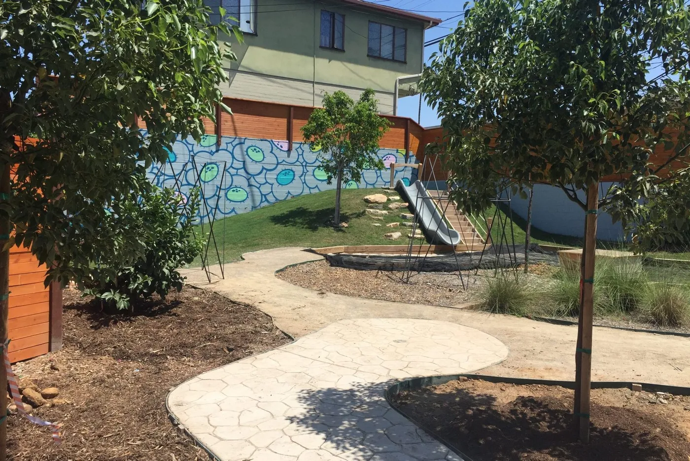 Landscaped play yard with a slide and a painted wall at Aspen Leaf Preschool