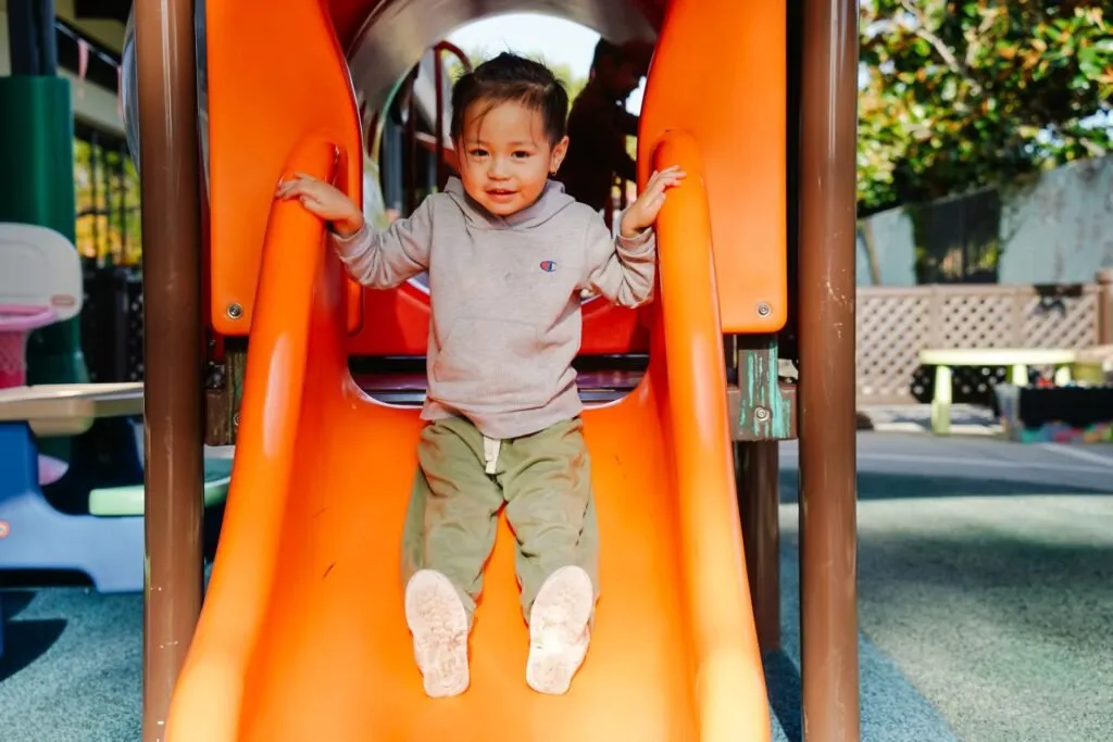A toddler at the bottom of an orange slide on the playground at Rock Academy Early Education