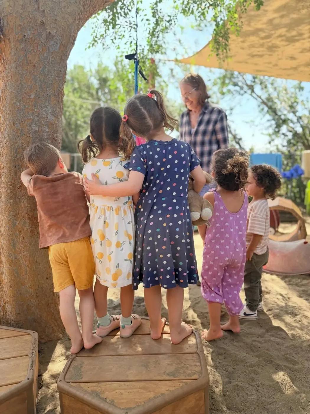 Children standing together in the sandy play yard at San Diego Cooperative Preschool