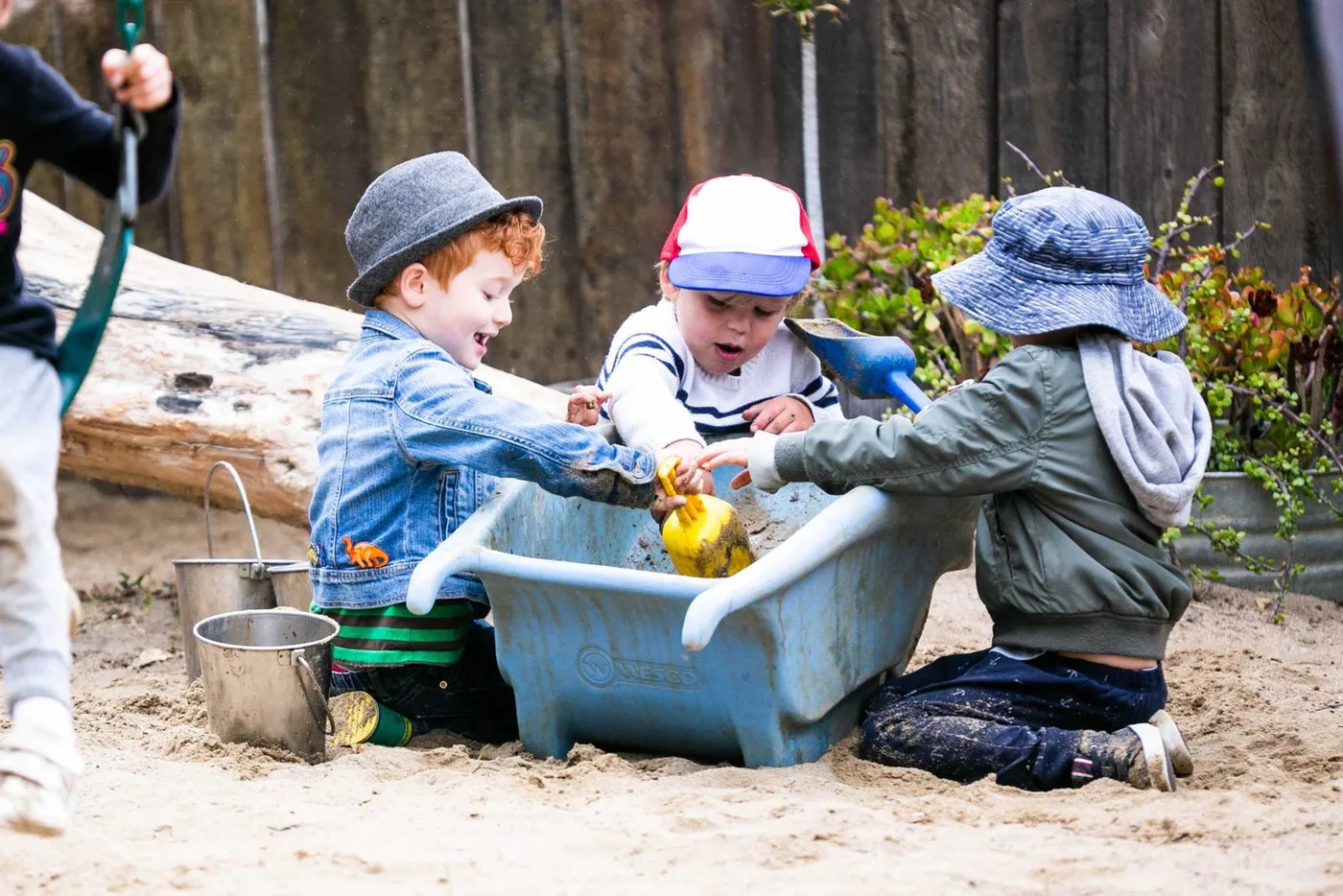 Three children playing with water in a sand area at the Waldorf School of San Diego